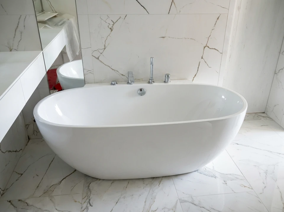 Un plombier en casquette bleue et combinaison de travail répare un robinet mélangeur de baignoire dans une salle de bains carrelée blanche