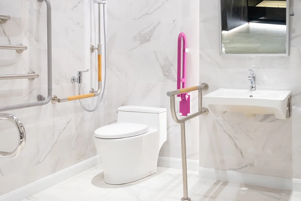 Salle de bain adaptée PMR avec toilettes suspendues blanches équipées de barres d'appui rabattables en acier inoxydable