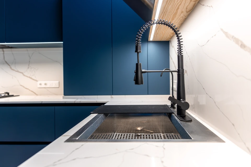Une personne en chemise rayée mesure avec une règle métallique graduée l'espace entre un lavabo moderne blanc et un mur dans une salle de bain contemporaine aux tons beiges