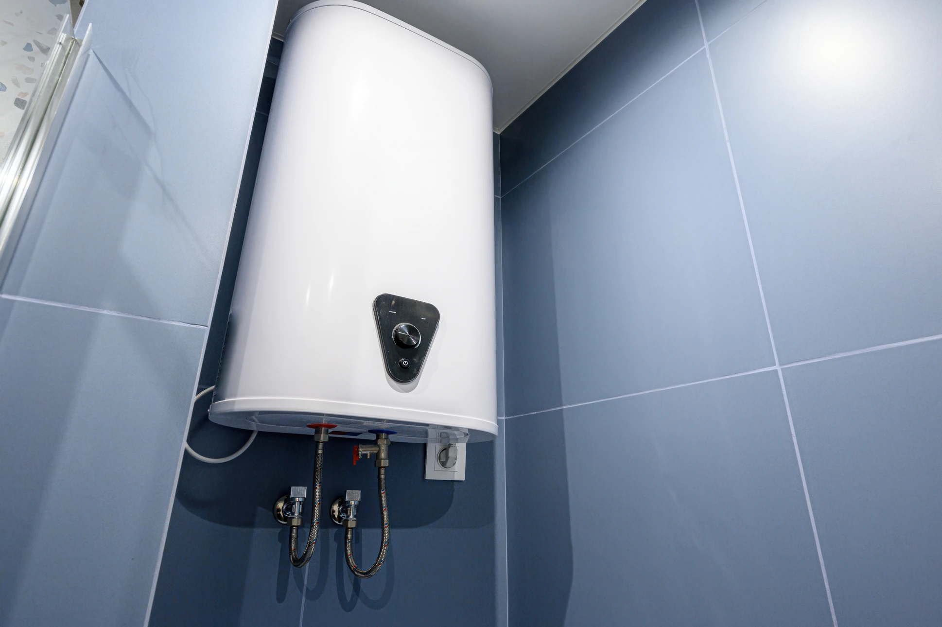 Toiture résidentielle équipée de quatre chauffe-eau solaires thermiques installés sur tuiles rouges, ciel bleu dégagé en arrière-plan avec maisons voisines visibles